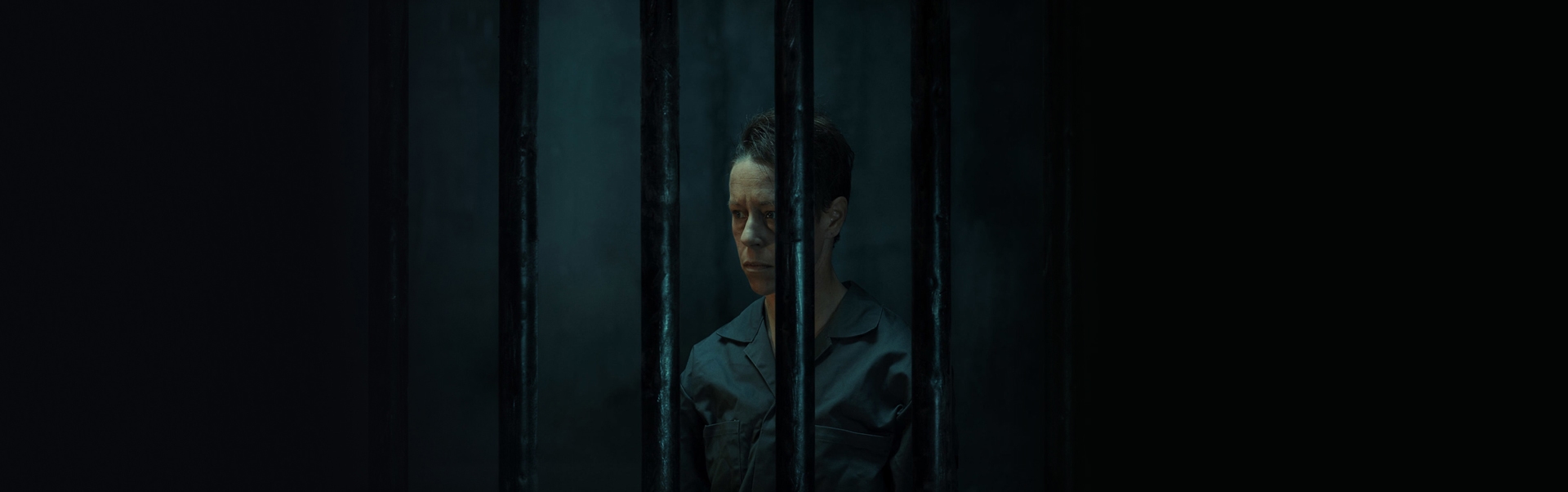 A non-binary person in a dark jail cell