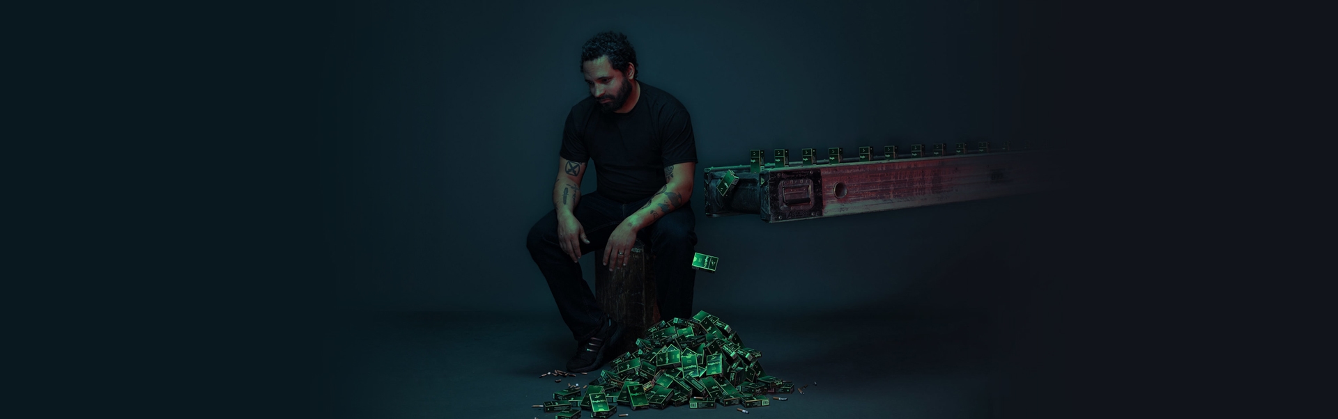 A man sitting on a stool in a dark space next to a conveyor belt dropping off cigarette cartridges