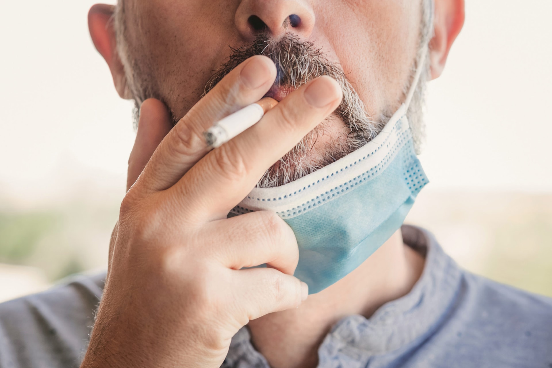 closeup of a person smoking a cigarette, with their COVID masked pulled down