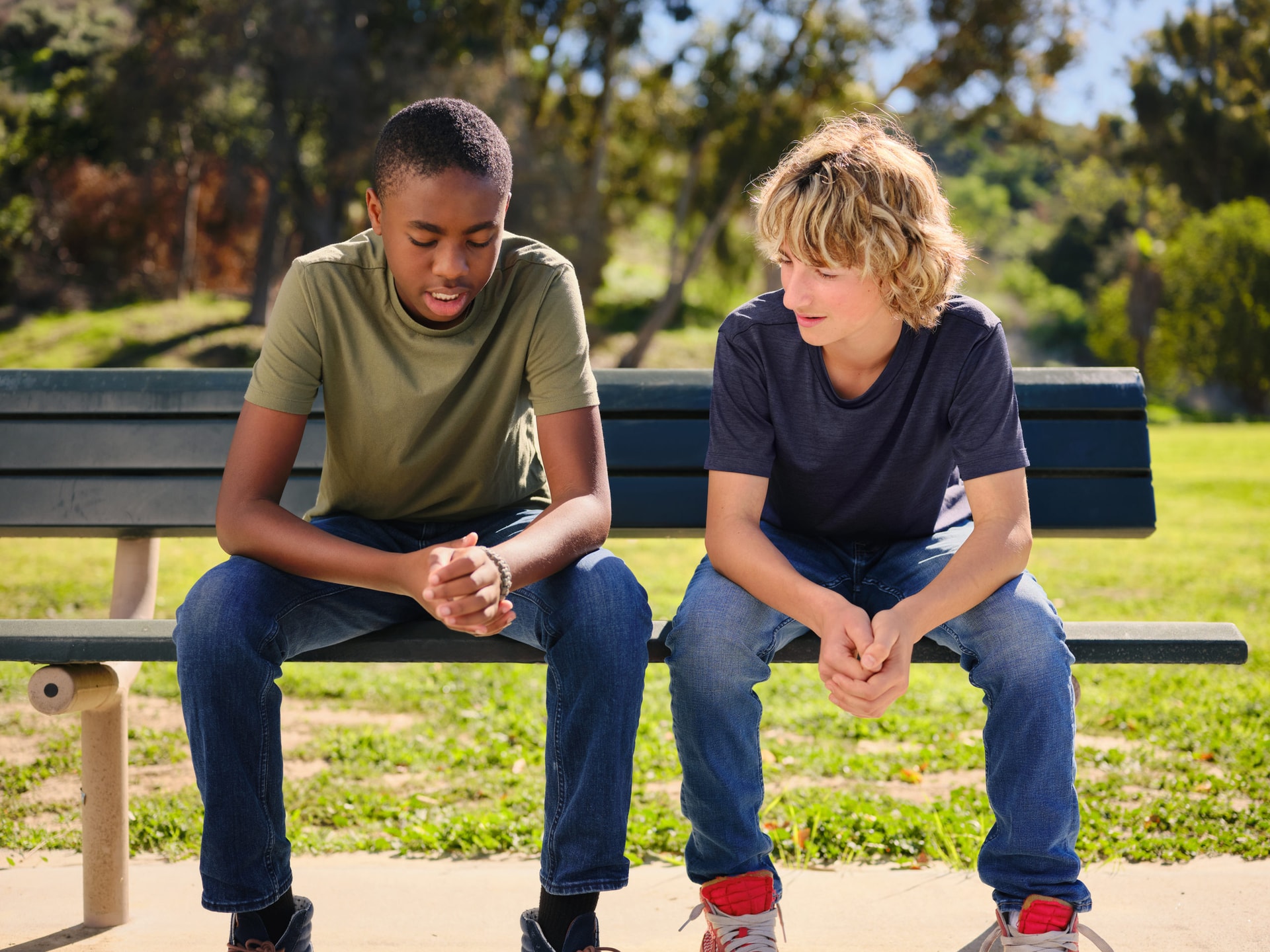 two teenage boys talk to each other on a park bench