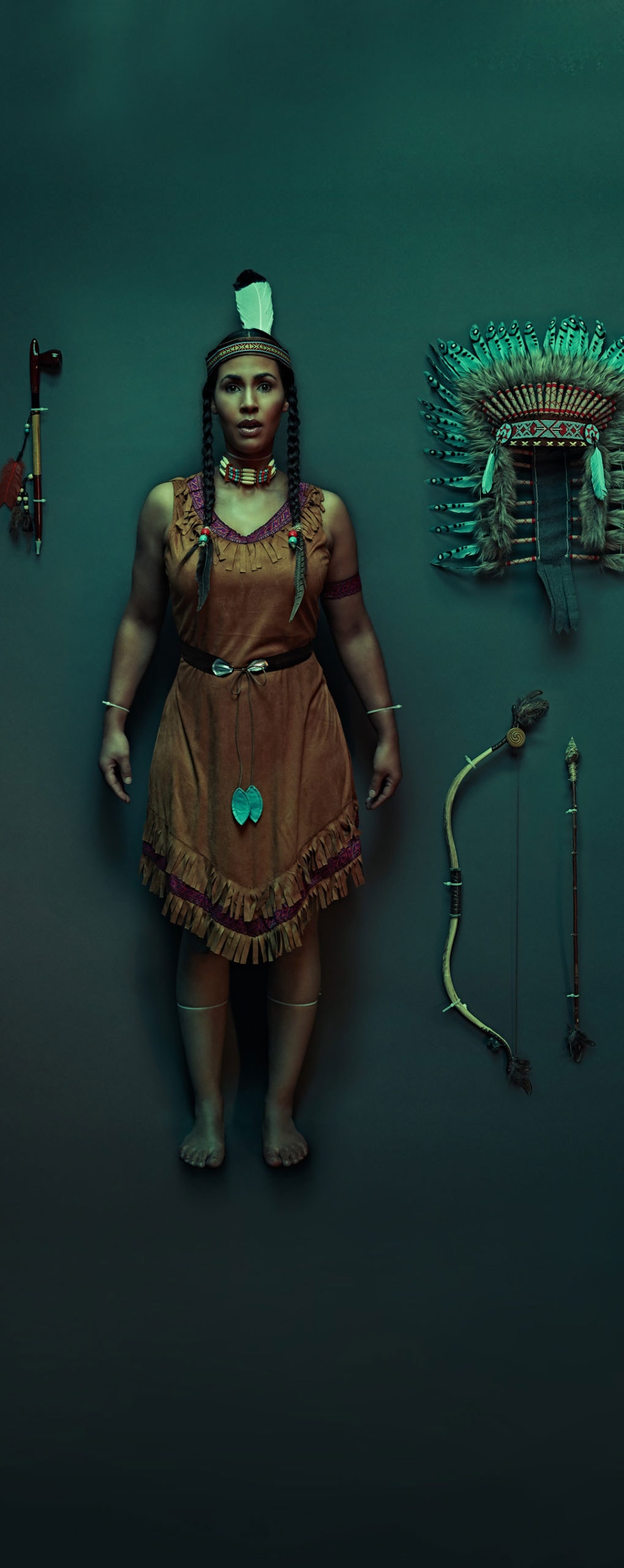 An American Indian woman dressed in traditional clothing standing in a dark room with American Indian accessories on display