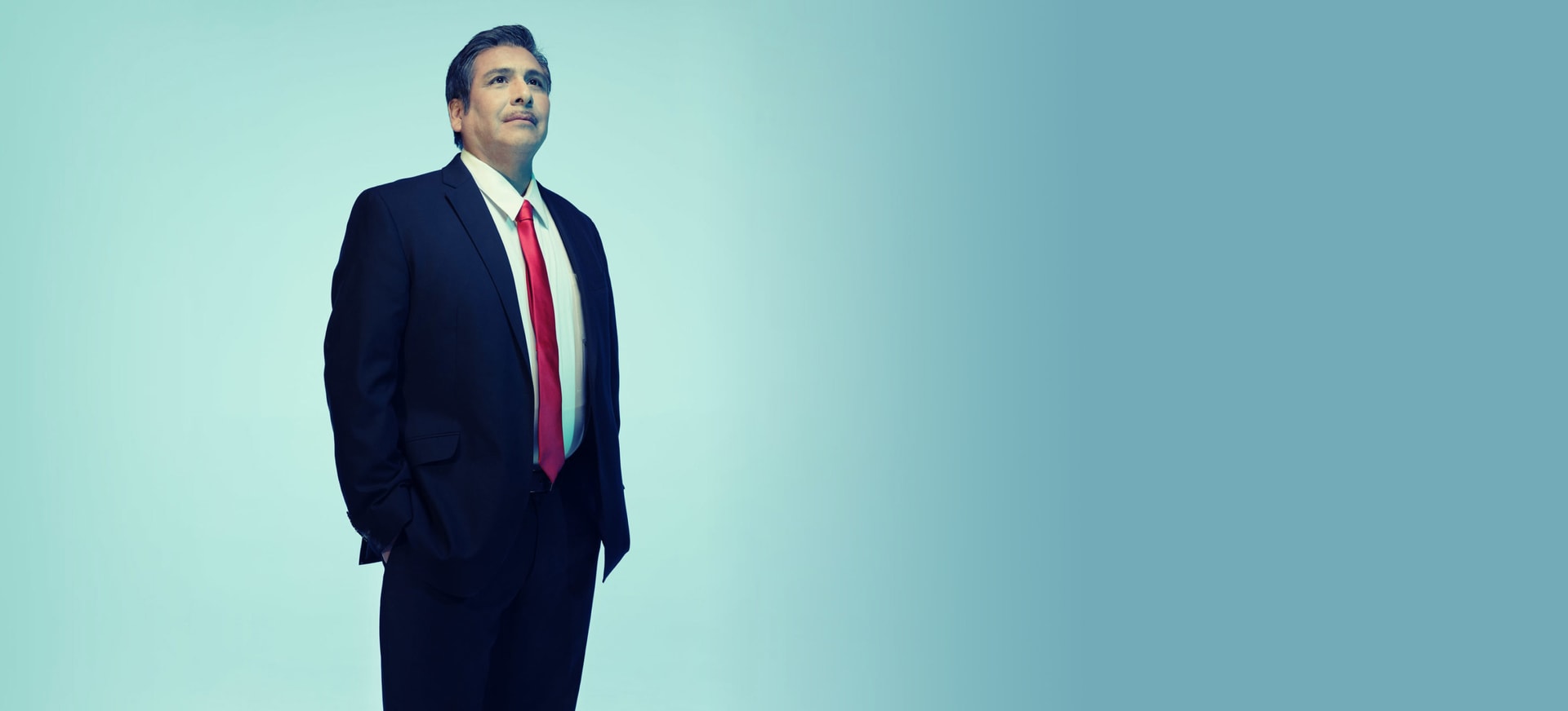 A Hispanic/Latino man in a suit standing in a light background