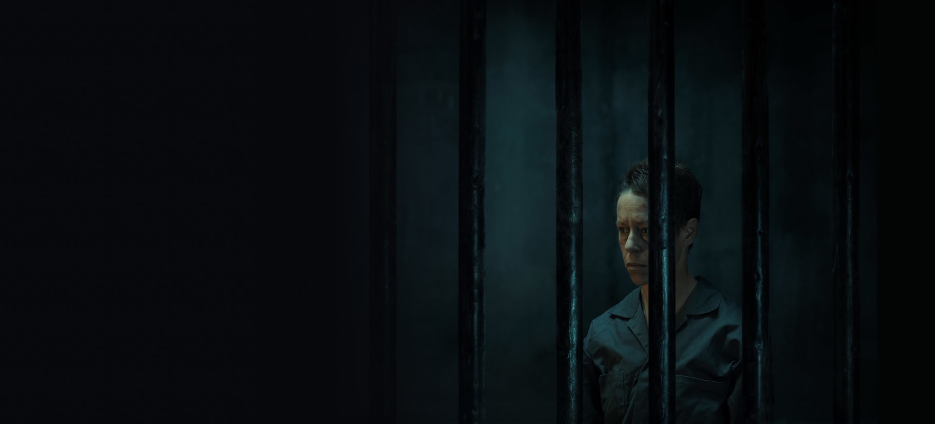 A non-binary person in a dark jail cell room