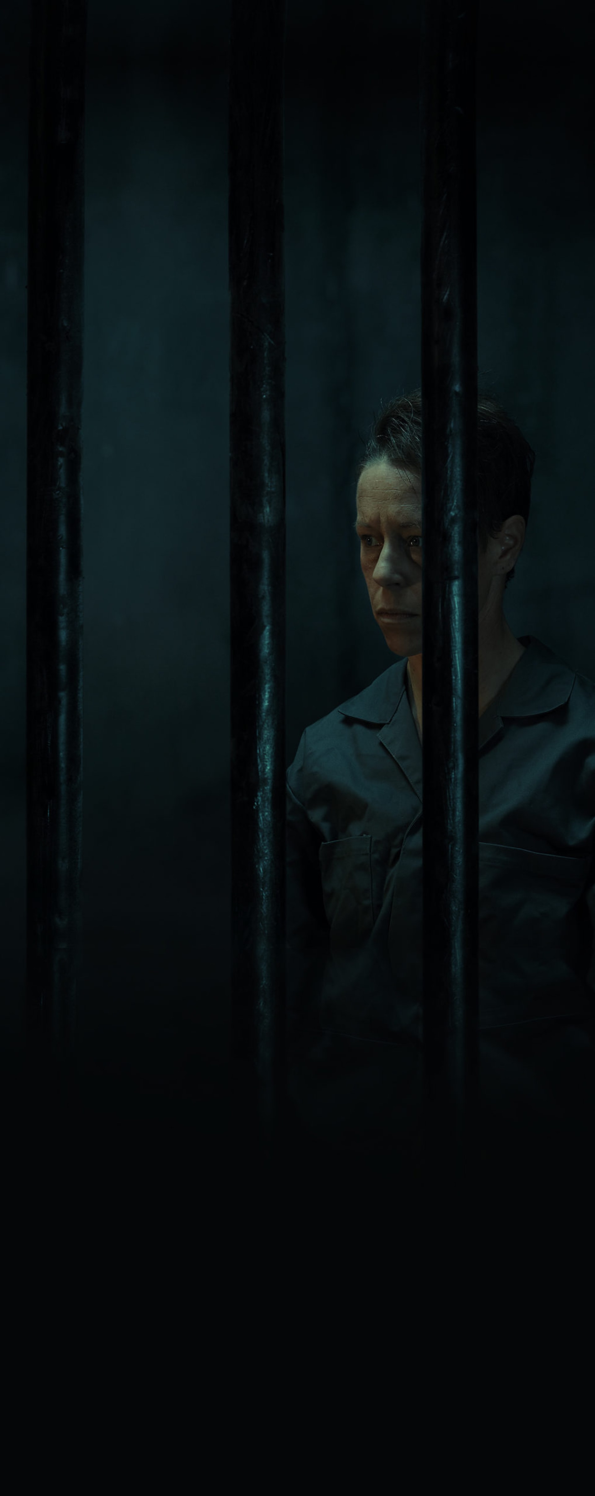 A non-binary person in a dark jail cell room