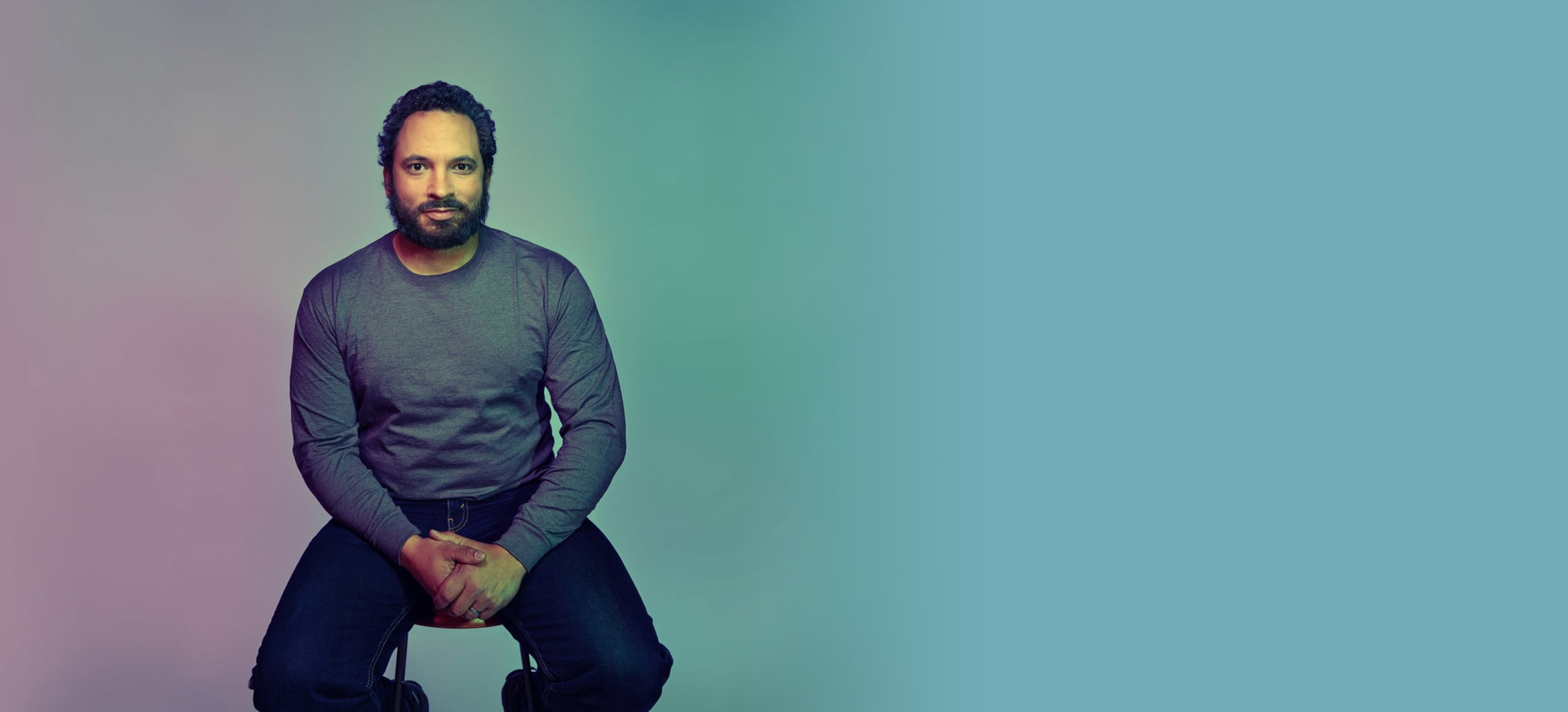 A man sitting on a stool in a light background
