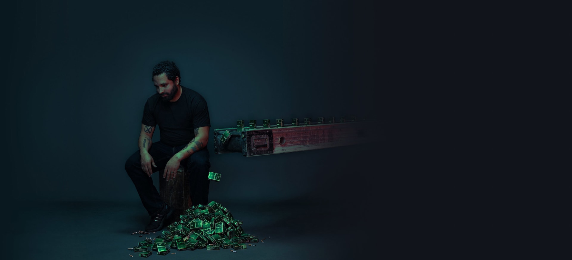 A man sitting on a stool in a dark space next to a conveyor belt dropping off cigarette cartridges