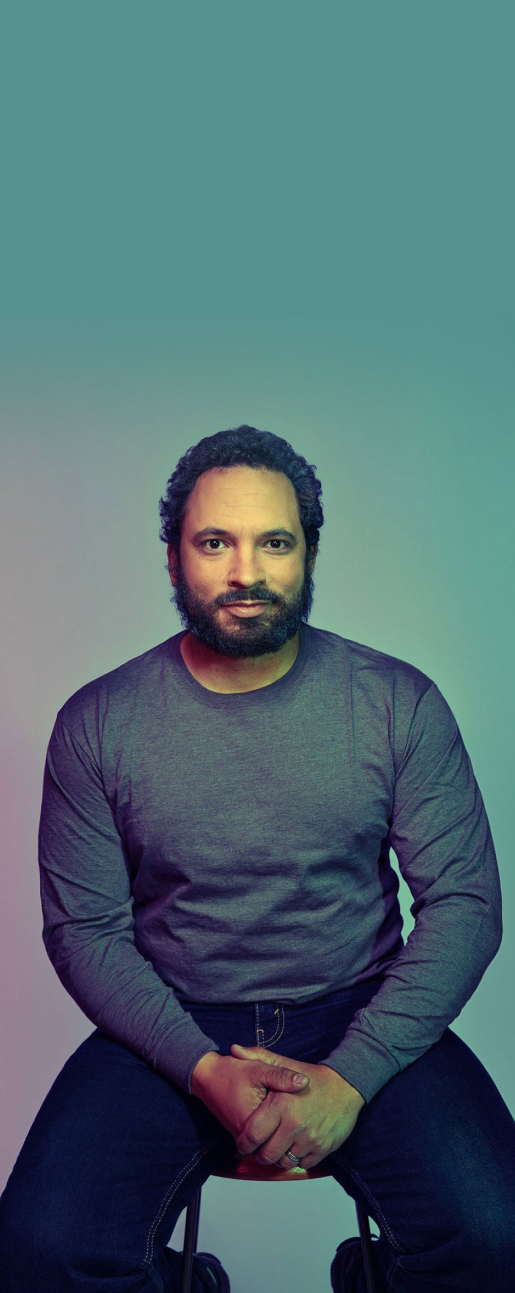 A man sitting on a stool in a light background