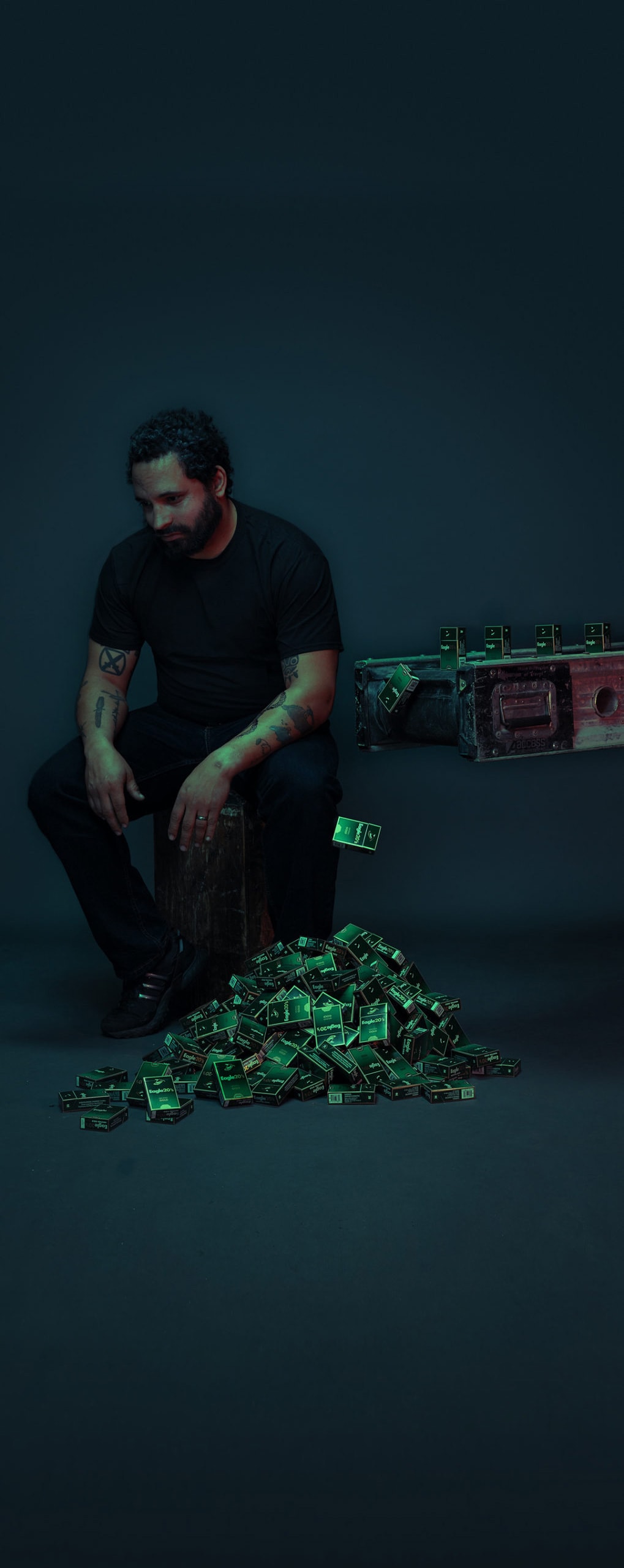 A man sitting on a stool in a dark space next to a conveyor belt dropping off cigarette cartridges