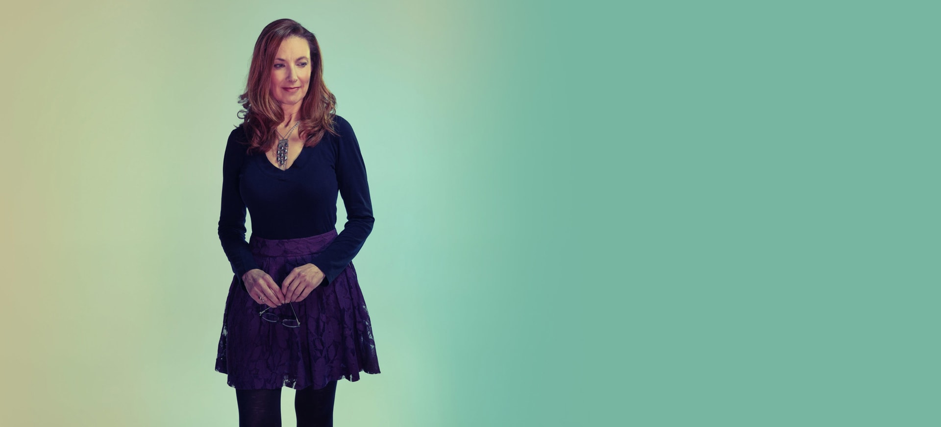 A woman in a skirt standing and smiling with a light background