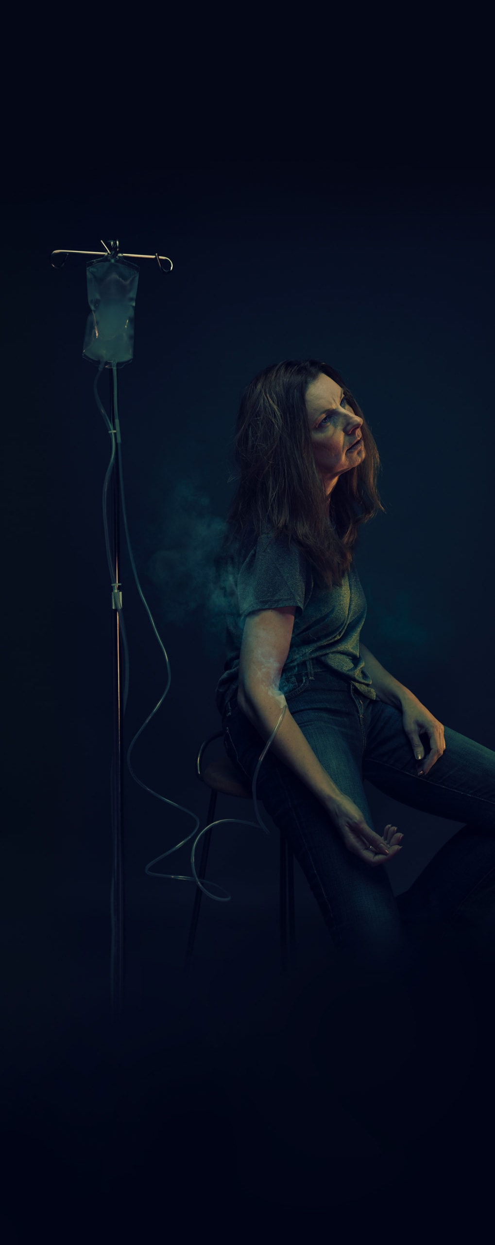 Woman sitting in the dark with IV bag filled with smoke
