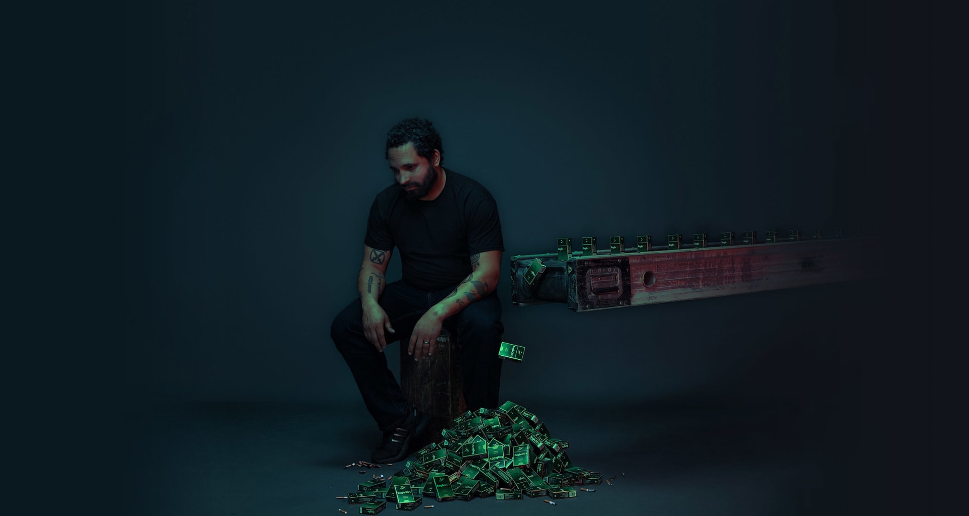 A man sitting on a stool in a dark space next to a conveyor belt dropping off cigarette cartridges