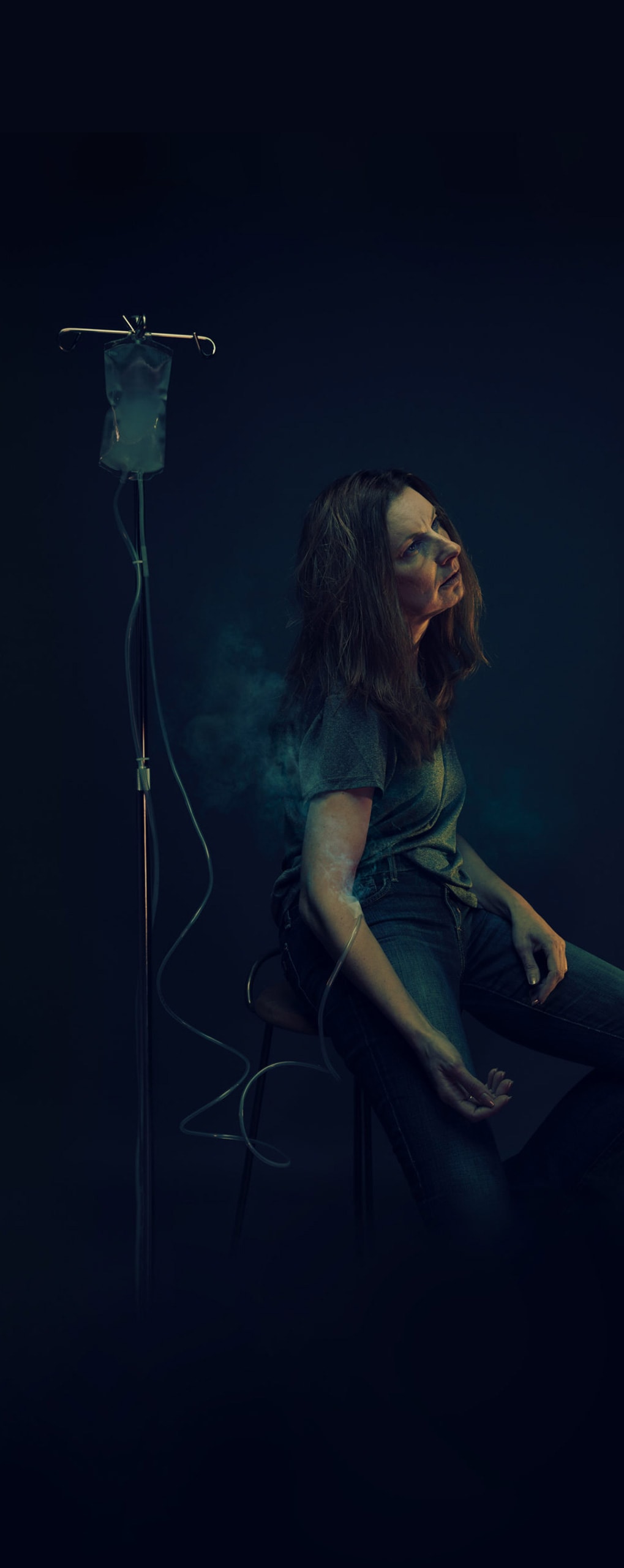 A woman sitting down with a IV in her arm filled with smoke