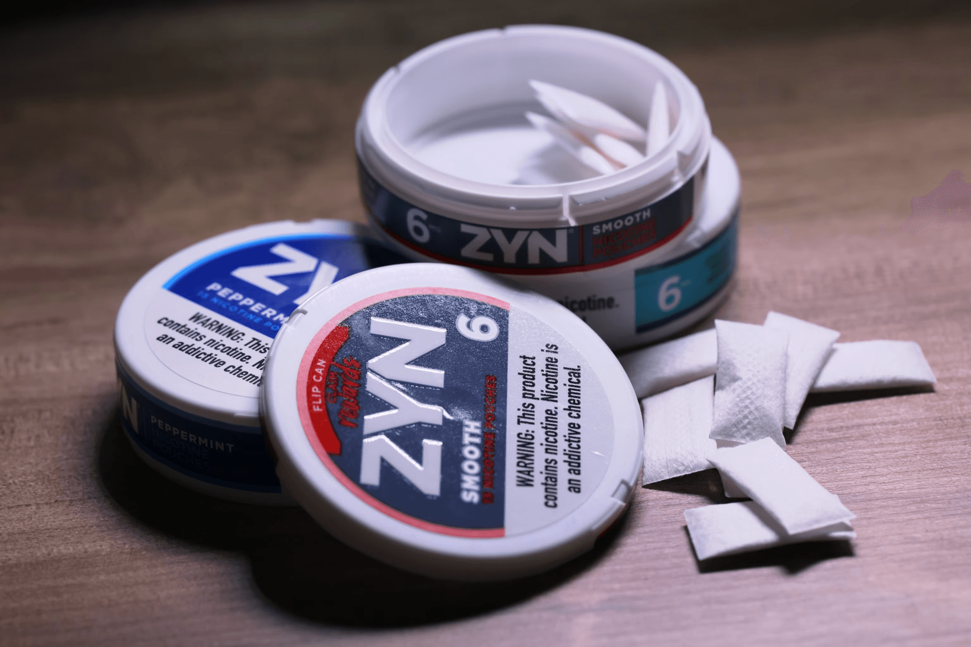 An image of Zyn containers and oral nicotine pouches displayed on a table, showing the warning label that reads: This product contains nicotine. Nicotine is an addictive chemical.