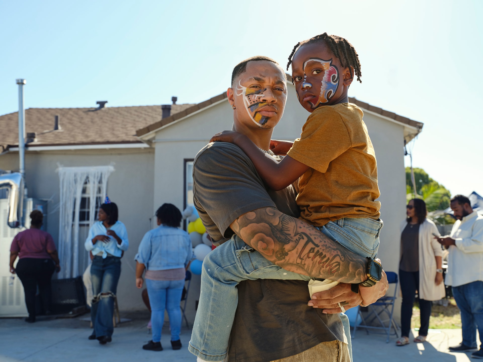 Isaiah, an African American father, holding his son in his arms with their faces painted from a party
