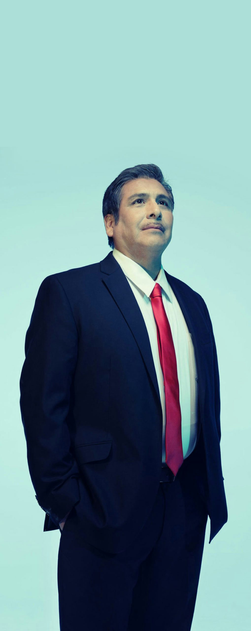 A Hispanic/Latino man in a suit standing in a light background
