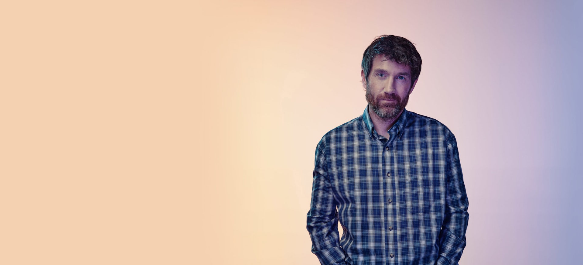 Man in plaid shirt standing with a light background behind him