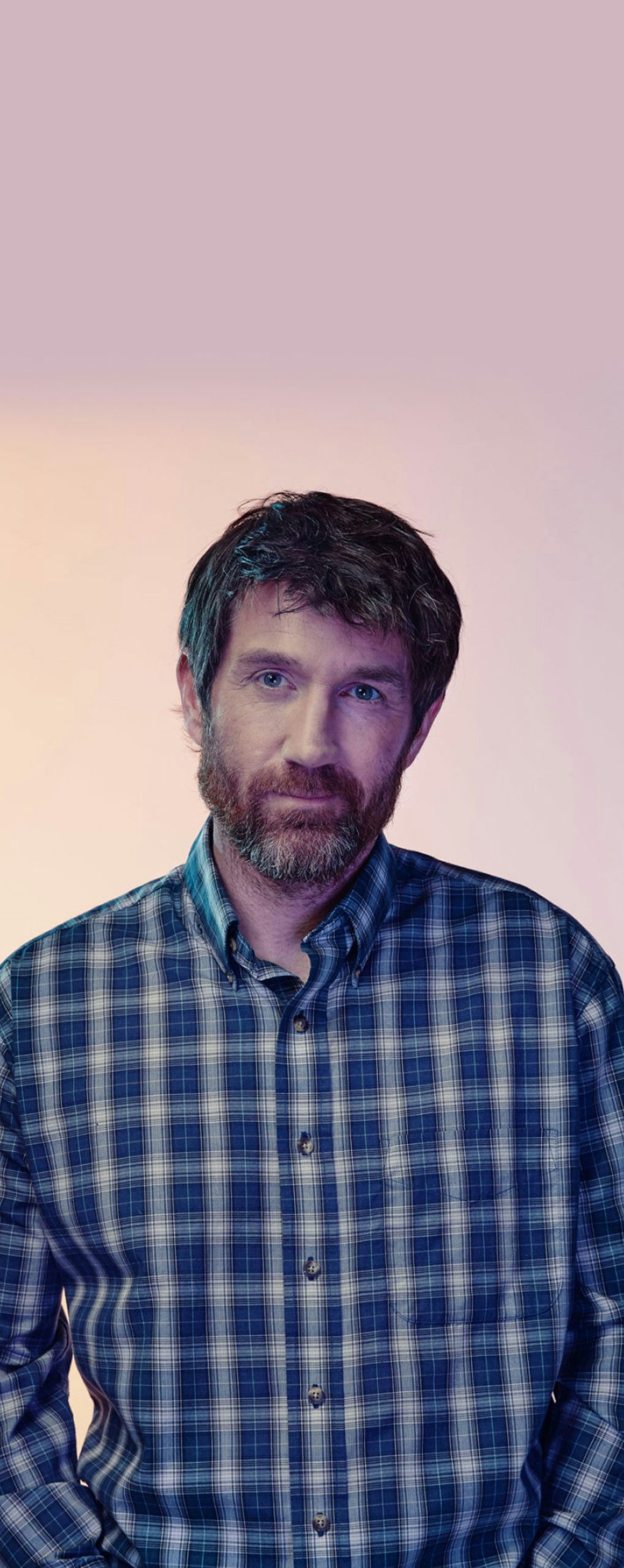 Man in plaid shirt standing with a light background behind him