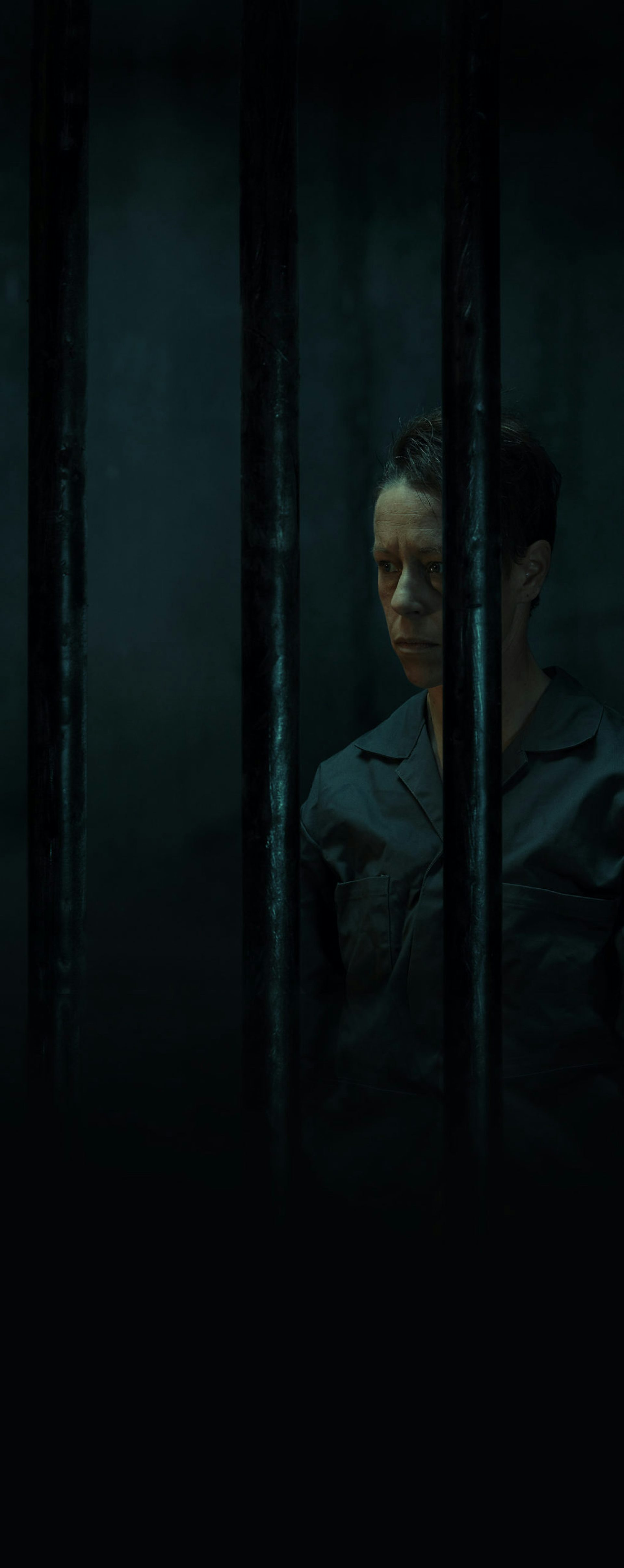 A non-binary person in a dark jail cell