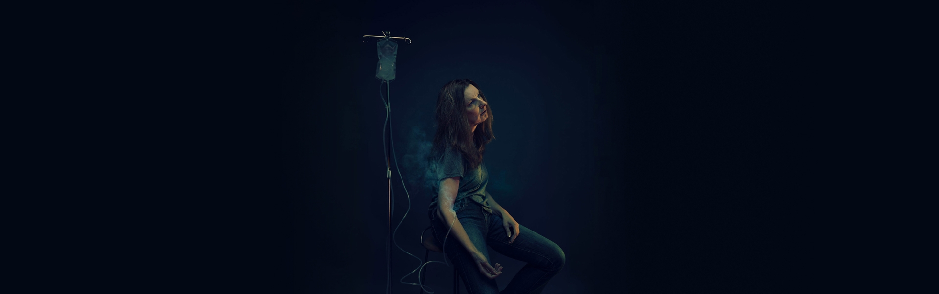 A woman sitting down with a IV in her arm filled with smoke